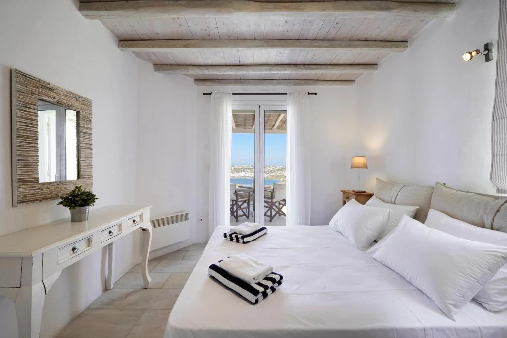 A bright double bedroom with white linen, natural beams and a balcony